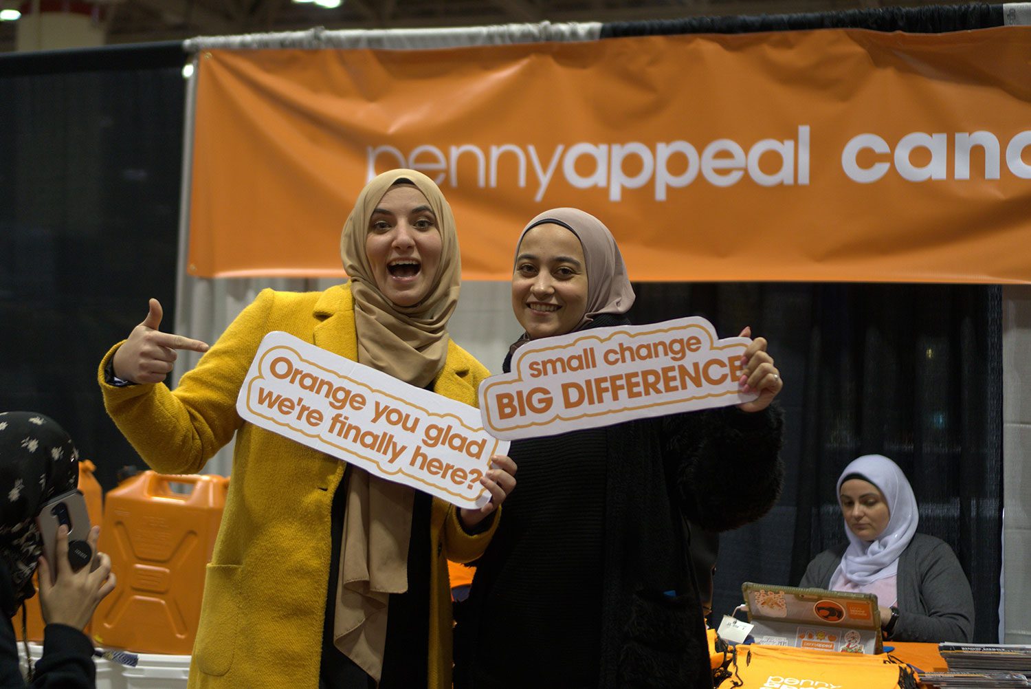 Team Orange volunteers smiling and holding signs that read 'Orange you glad we're finally here?' and 'Small Change, Big Difference'